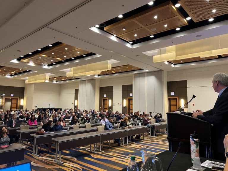 man behind podium presenting to a room full of people