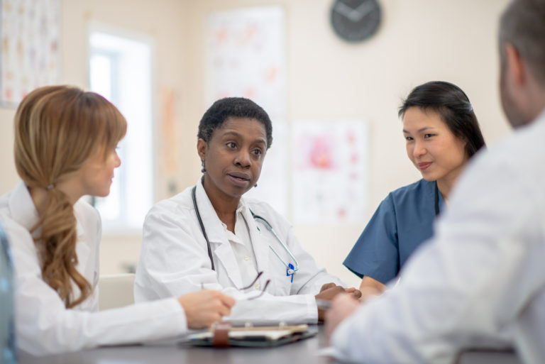 A group of healthcare workers consisting of doctors and nurses are meeting together at their hospital.