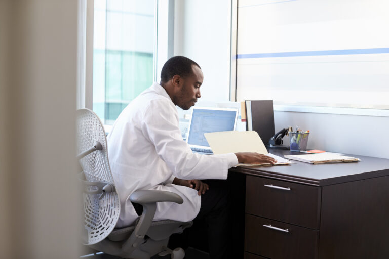 Doctor Wearing White Coat Reading Notes In Office